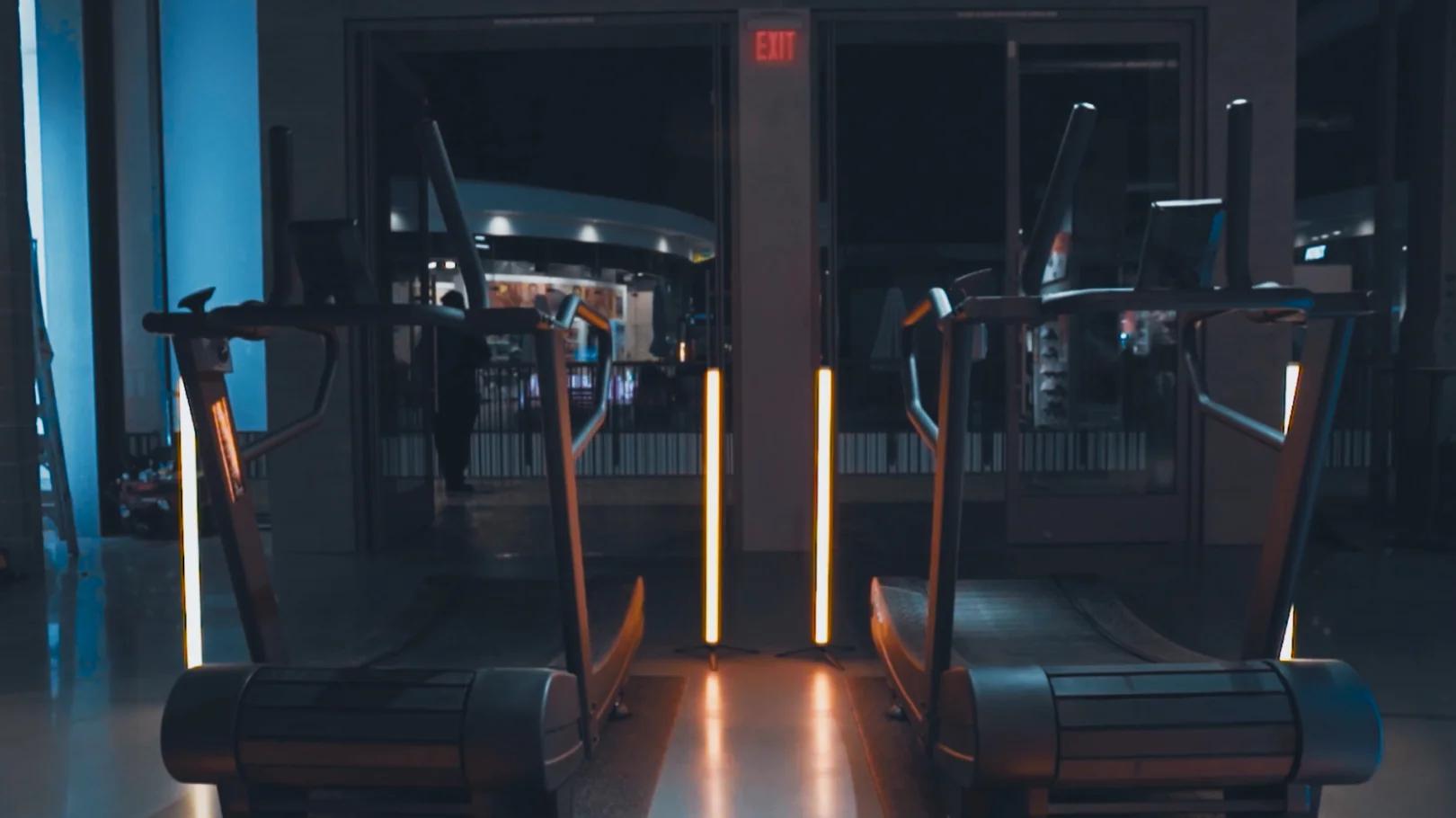 dramatically lit treadmills with large orange tube lights reflecting off the dark floor