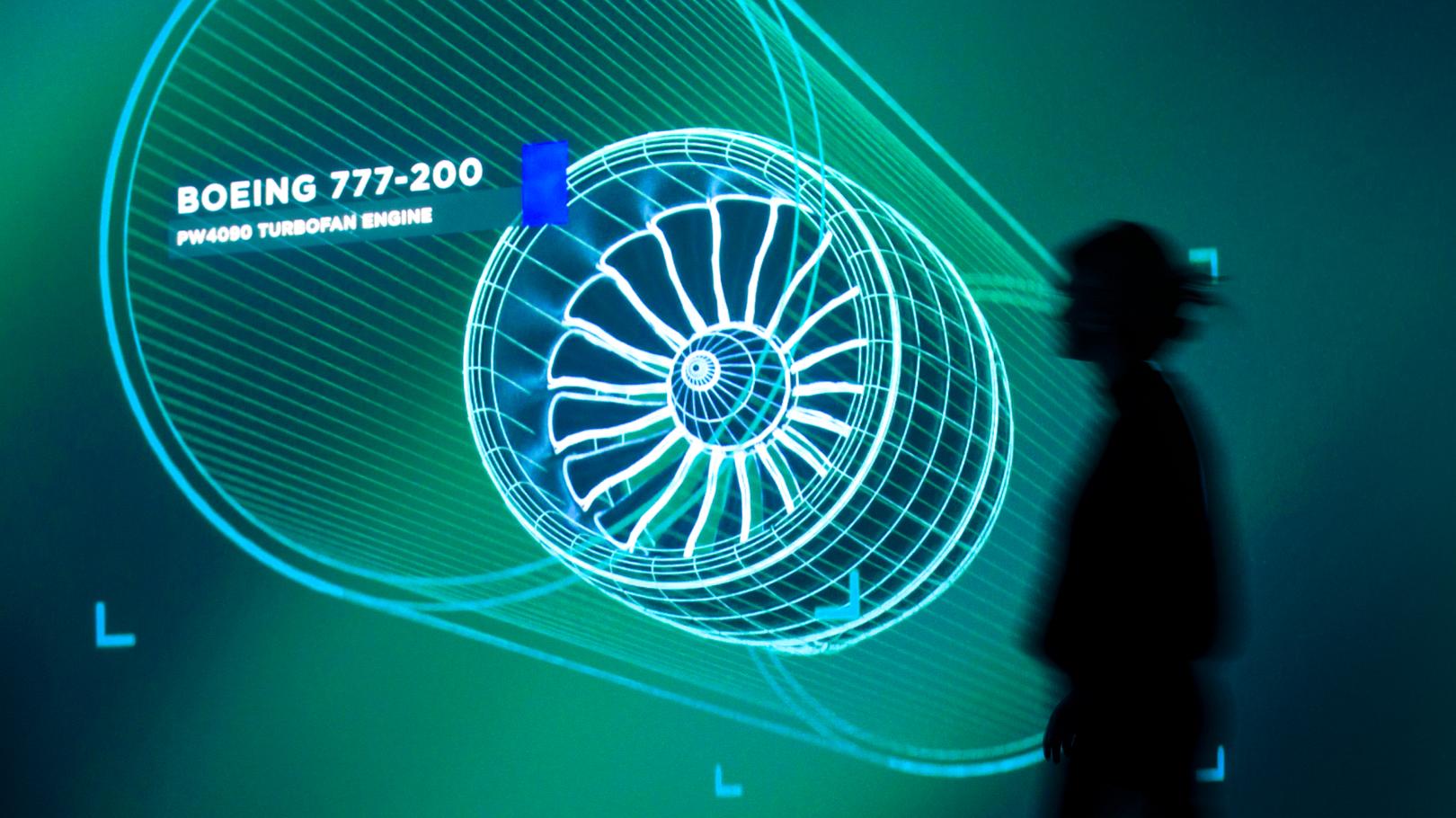 Woman in silohuette in front of a large green glowing image of an airplane engine CAD drawing