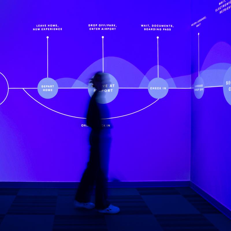 one person, blurred, standing in silhouette in front of a glowing blue wall with a data-visualization timeline across it